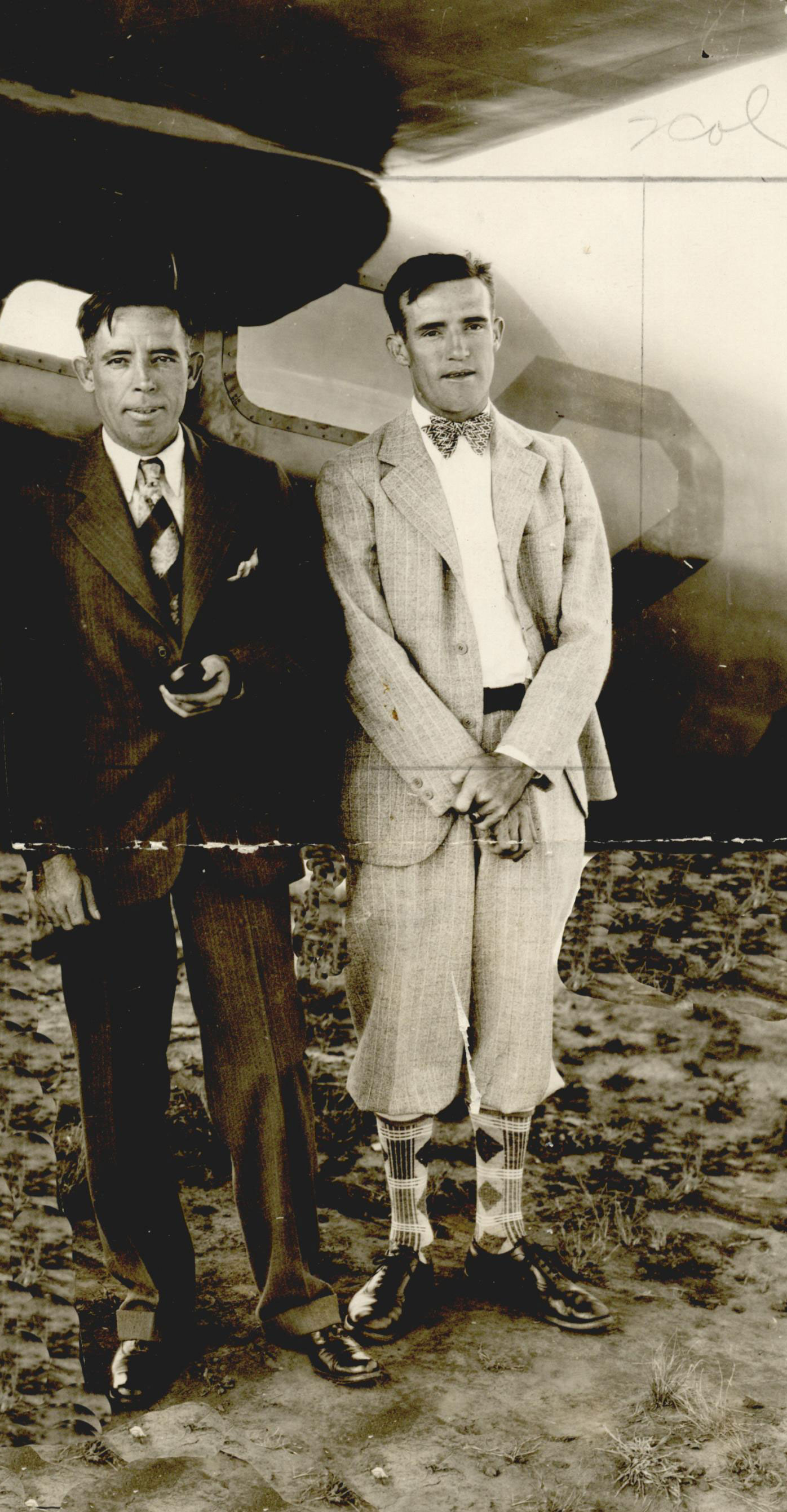Earl and John Haliburton stand in front of a small aircraft. They both wear suits and ties and look directly into the camera.