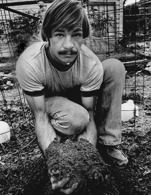 A kneeling man holds a large pile of dirt in both hands.