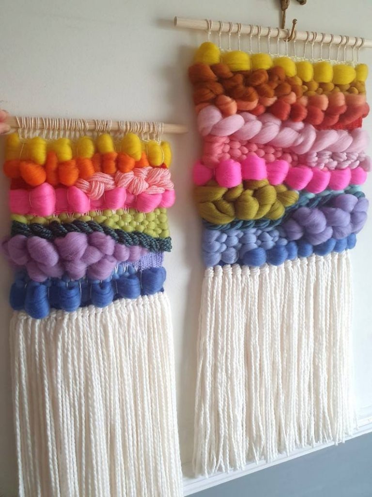 Brightly colored wall-handing with yellow, orange, pink, green, purple, and blue fiber in varying thicknesses above a long white fringe. 