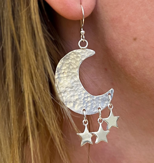 Silver-colored dangling moon-shaped earrings with three small stars hanging form the bottom