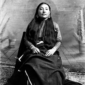 A woman in traditional dress is seated in this black-and-white historical photograph. 