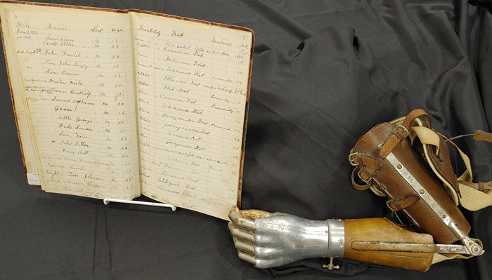 An 1896 ledger with hand-written entries, and a prosthetic hand made of metal with leather straps