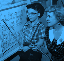 A teacher points to words on a sign as a young girl looks on