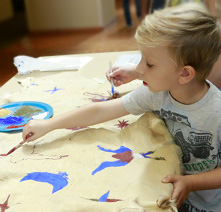 A young boy paints on a large piece of leather