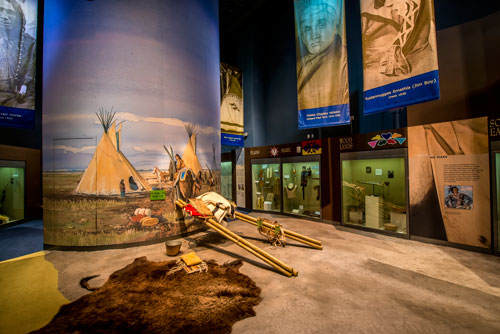 Part of an exhibit with a small tipi mural next to a bison hide rug