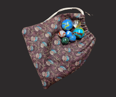 Glass marbles in various sizes and colors on top of a fabric drawstring bag.