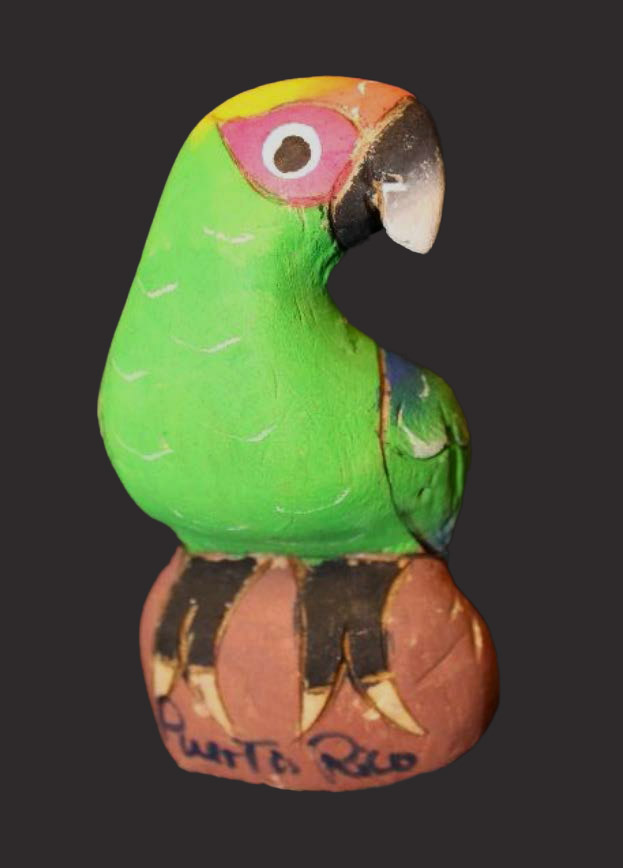 A brightly colored clay parrot sits on a rock painted with the words Puerto Rico.