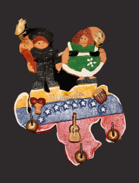 Ceramic with two people on the shape of Venezuela, which is covered with stars, stripes, and tiny instruments.