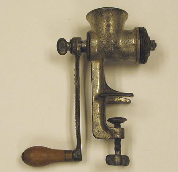 A metal tool with an opening at the top for the meat, a side handle, and a clamp to attach it to a surface. Ground meat is pushed out an opening on the opposite side of the handle.