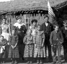 Students stand before a sod schoolhouse 