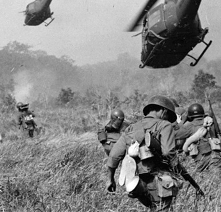 Soliders advance through tall grass as helicopters fly closely overhead
