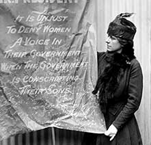 A woman stands holding a large banner advocating for women's suffrage 