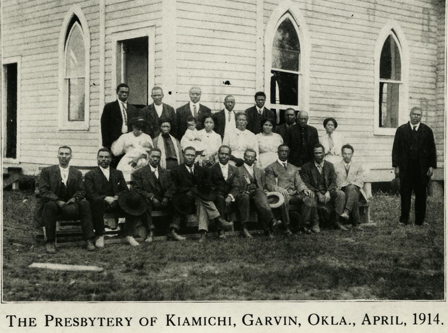 A group portrait of around 25 African American church members outside the large wooden church building. 