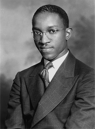 A photograph of an African American man with glasses, sitting with a small smile.