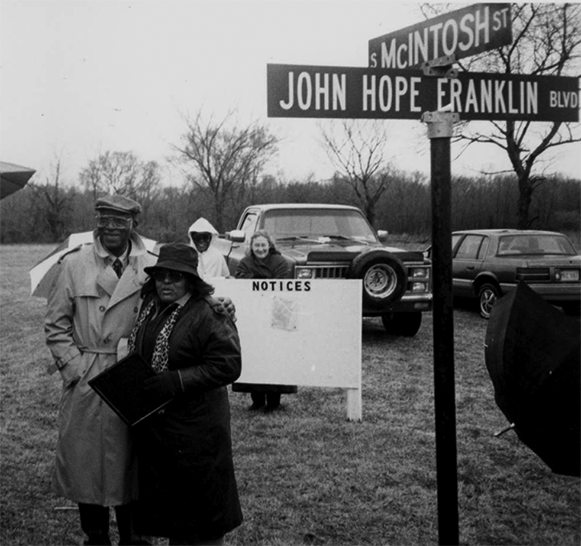 A photograph of people, two men in the foreground, standing next to a street sign that says JOHN HOPE FRANKLIN BOULEVARD.