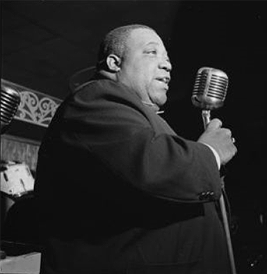 A Black man in a suit holds a microphone. 