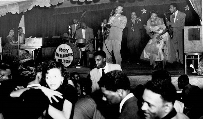 A band performs on a stage. In the foreground, several people are on the dance floor. 