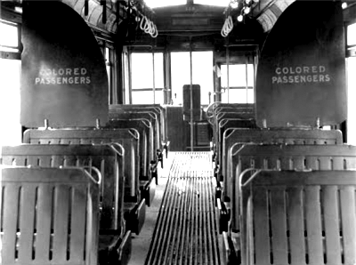 A Jim Crow-era photo of a segragated bus, with two signs indicating where the seats for Black passengers begin.