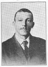 Newspaper photo of a Black Man with short hair and mustache in a suit. 