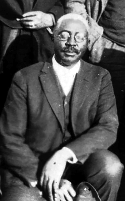 An African American man with a mustache and a slight smile looking at the camera.