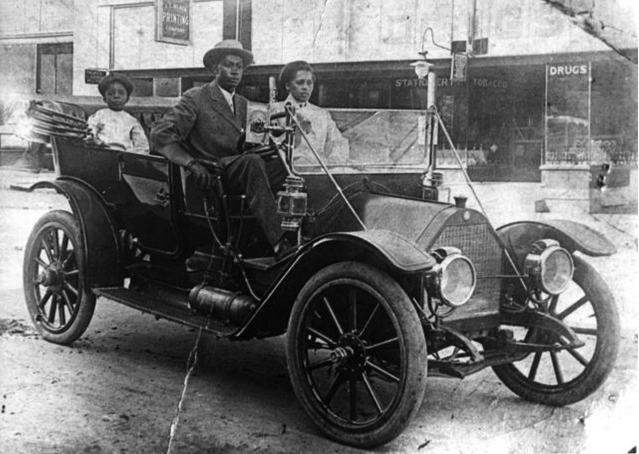 An African American family driving an automobile on a city street.