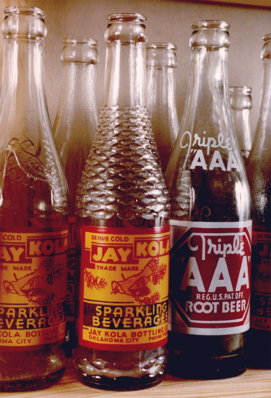 Three glass soda bottles with old-time styled labels on them. One reads, Jay Kola Sparkling Beverage and the other Triple AAA Root Beer.
