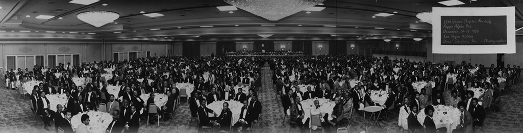 A panoramic shot of a banquet hall where a few hundred people sit at tables. 
