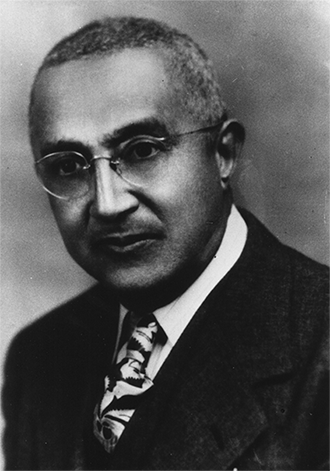 A closeup photograph of an African American man wearing glasses and a dark suit. 