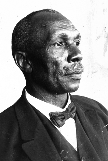 An older Black man with short hair and a mustache wearing a suit and a bow tie. 
