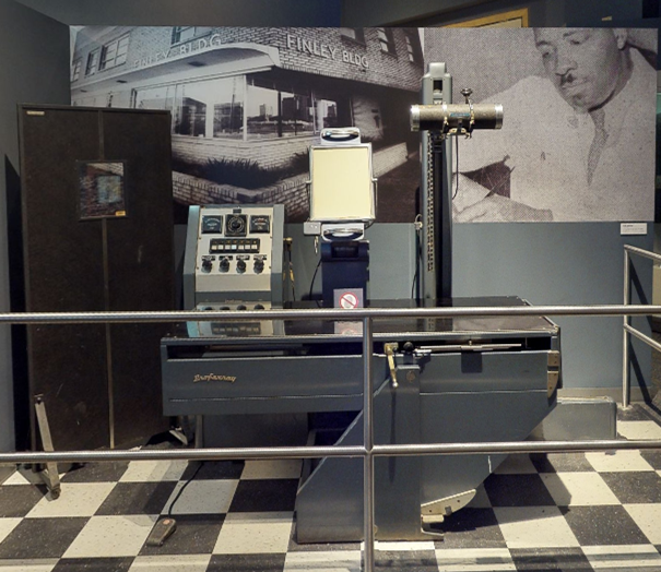 An older X-ray machine with enlarged historic photos behind it. This display is part of a museum exhibit.