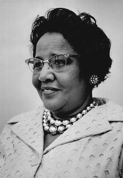A Black woman wearing a suit, glasses, and matching pearl earrlings and necklace. 