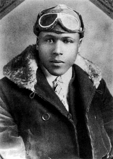 A young Black man wears a fur-lined coat, suit, and aviator cap. 