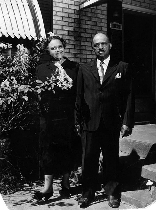 A older Black man and woman in front of a building. 