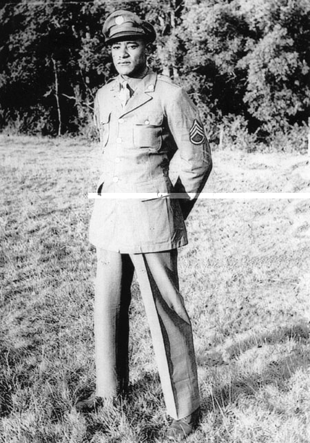 A Black man in an Army uniform stands in a field. 