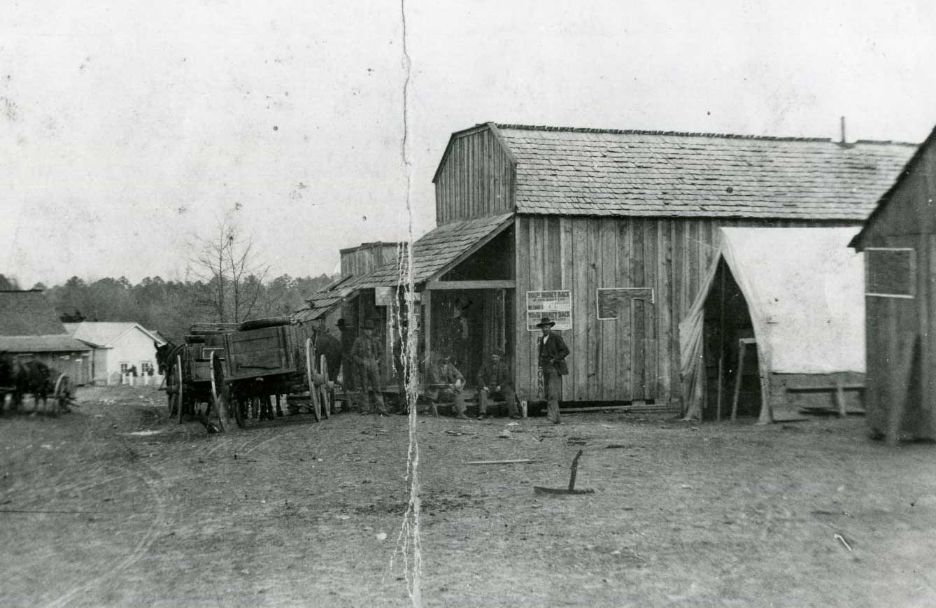 A small group of men and two horse-drawn wagons near a large wooden building.