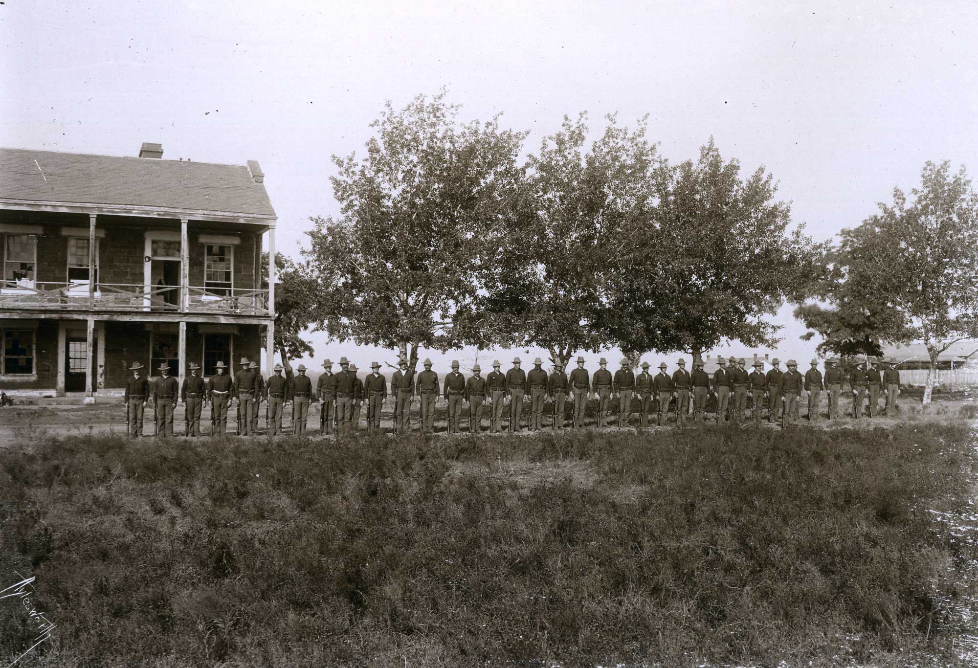 A long row of uniformed soldiers stand outside the commissary at Fort Gibson.
