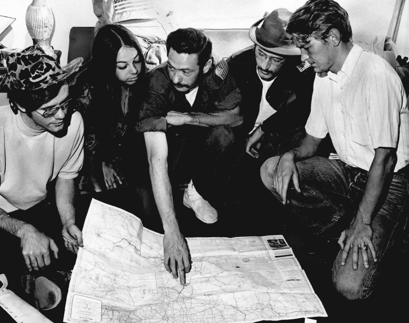 Five people kneel to examine a map of British Honduras on the ground. The man in the middle is pointing at a spot on the map. 