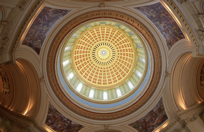 A view up into the interior of the Capitol dome, with arched niches displaying historic murals.