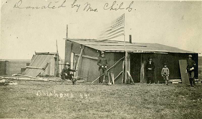 Five unknown people standing in front small wooden structure with the caption 'Oklahoma 89'