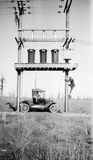 A man climbs a large, tall oil meter. A small car is parked underneath the meter.