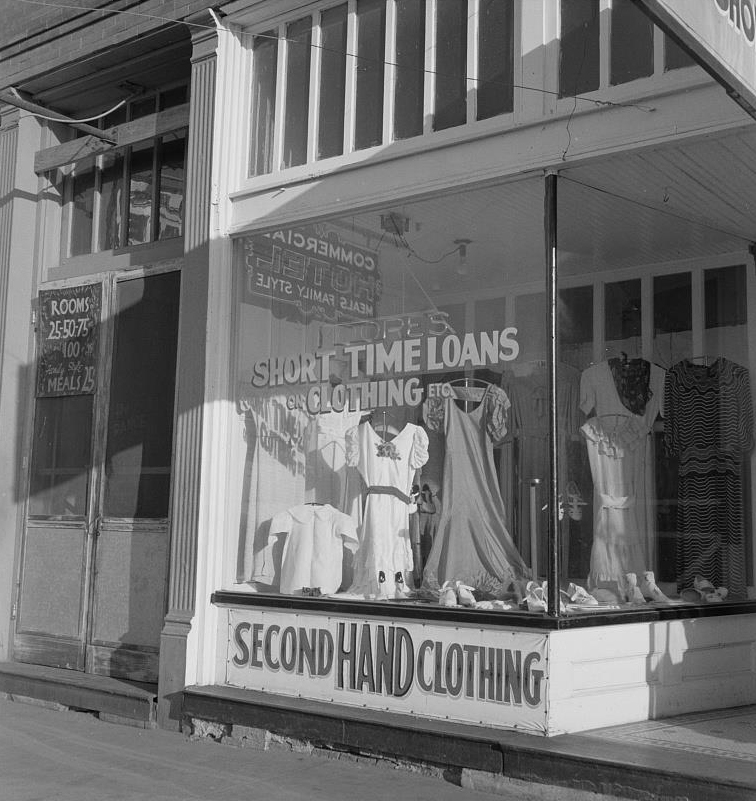 A store front advertises, 'Short term loans' and 'Second Hand Clothing' while the building next door has a sign that says, 'Rooms 25 cents, 50 cents, 75 cents, one dollar and meals 25 cents.'
