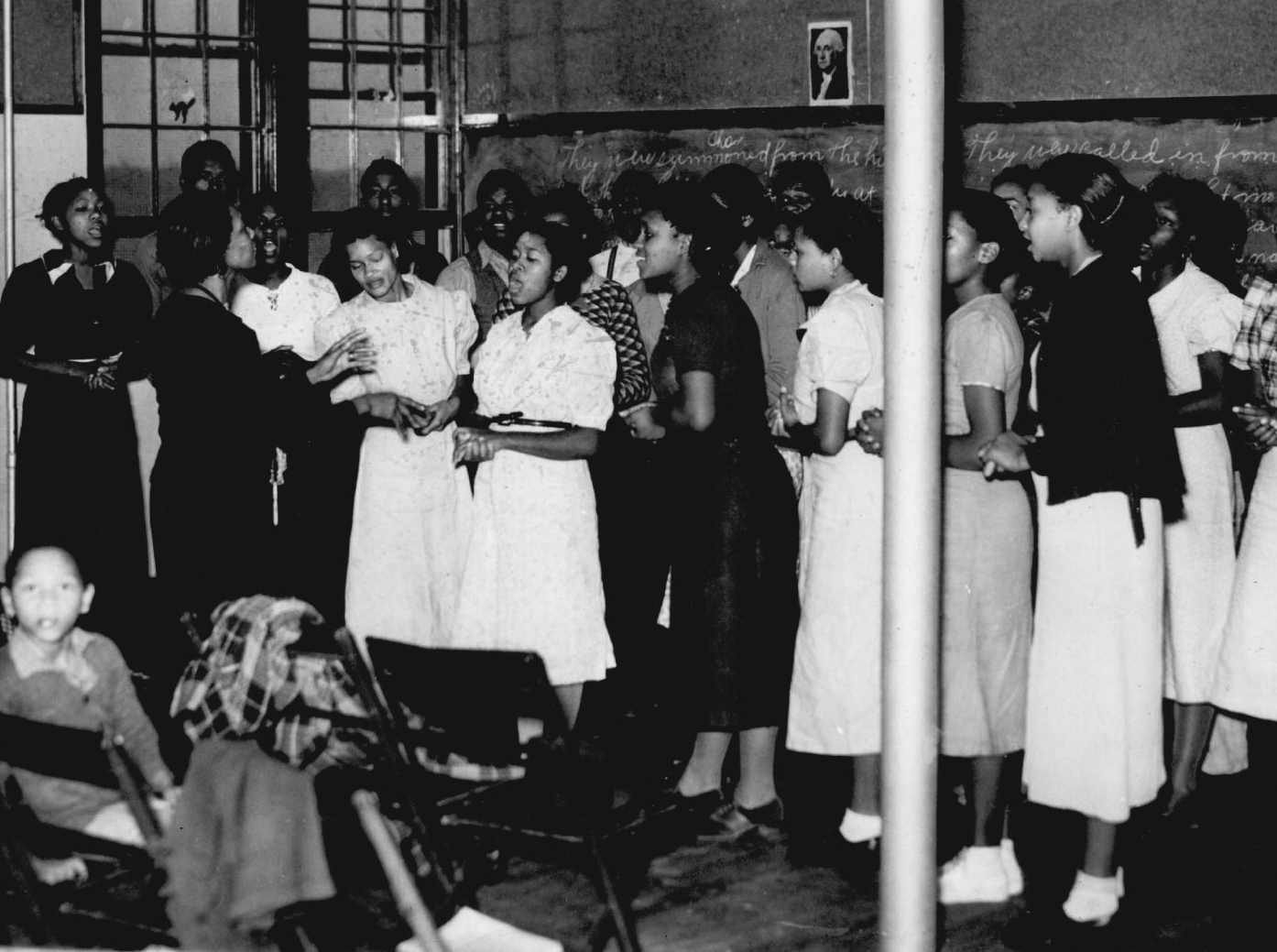 A group of young Black women sing while another woman stands in front of them conducting.