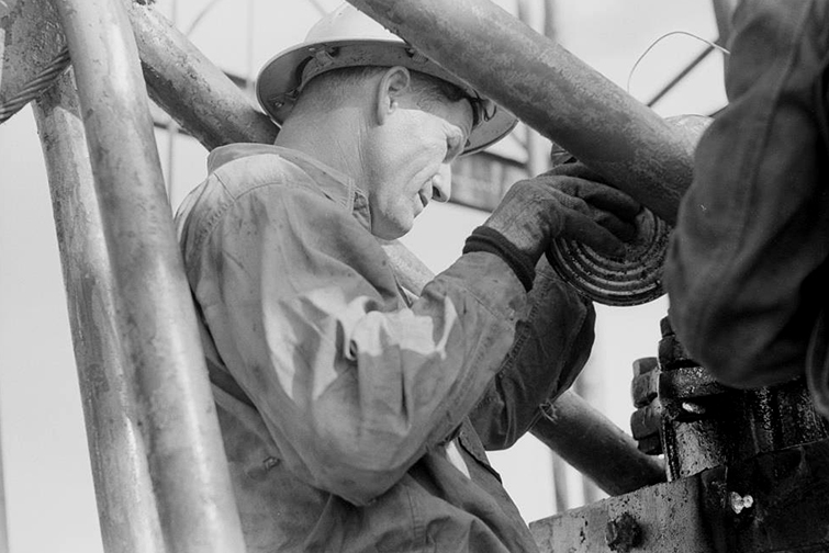A man in a hard hat and gloves works within some equipment. 
