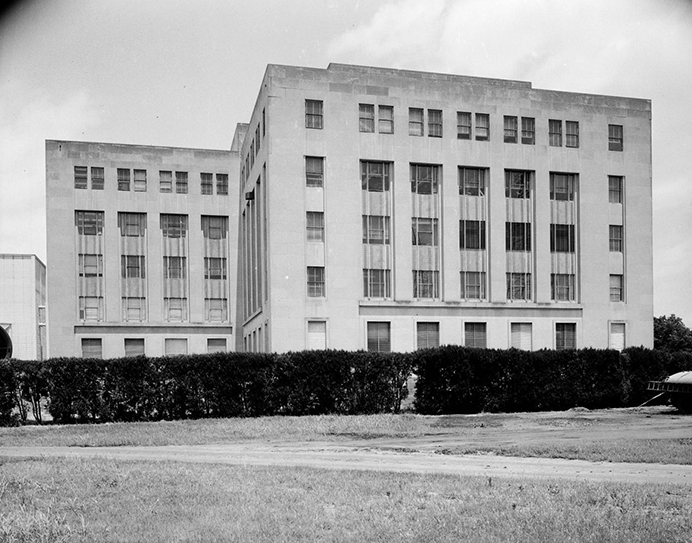 A large, five-story building with shrubs bordering the front of the entire structure. 