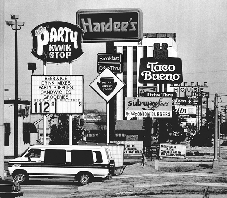 A cluster of fast food restaurant and convenience store signs, including Party Quik Stop, Hardees, Taco Bueno, Subway, and Waffle House. 
