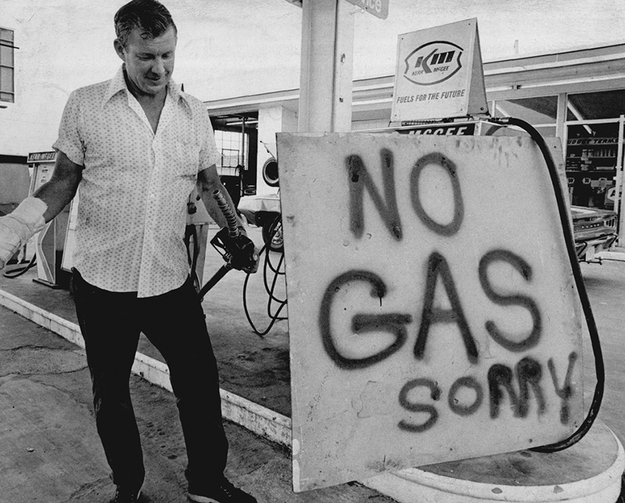 A man stands at a gas pump next to a hand-written sign that reads, no gas, sorry
