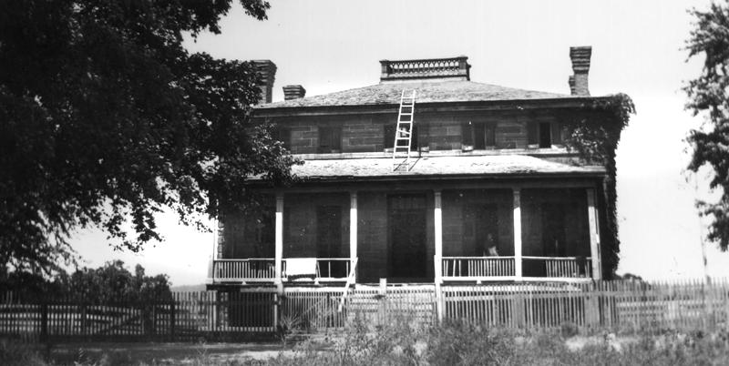 Historic black-and-white photograph of a multistory brick building with a large porch.
