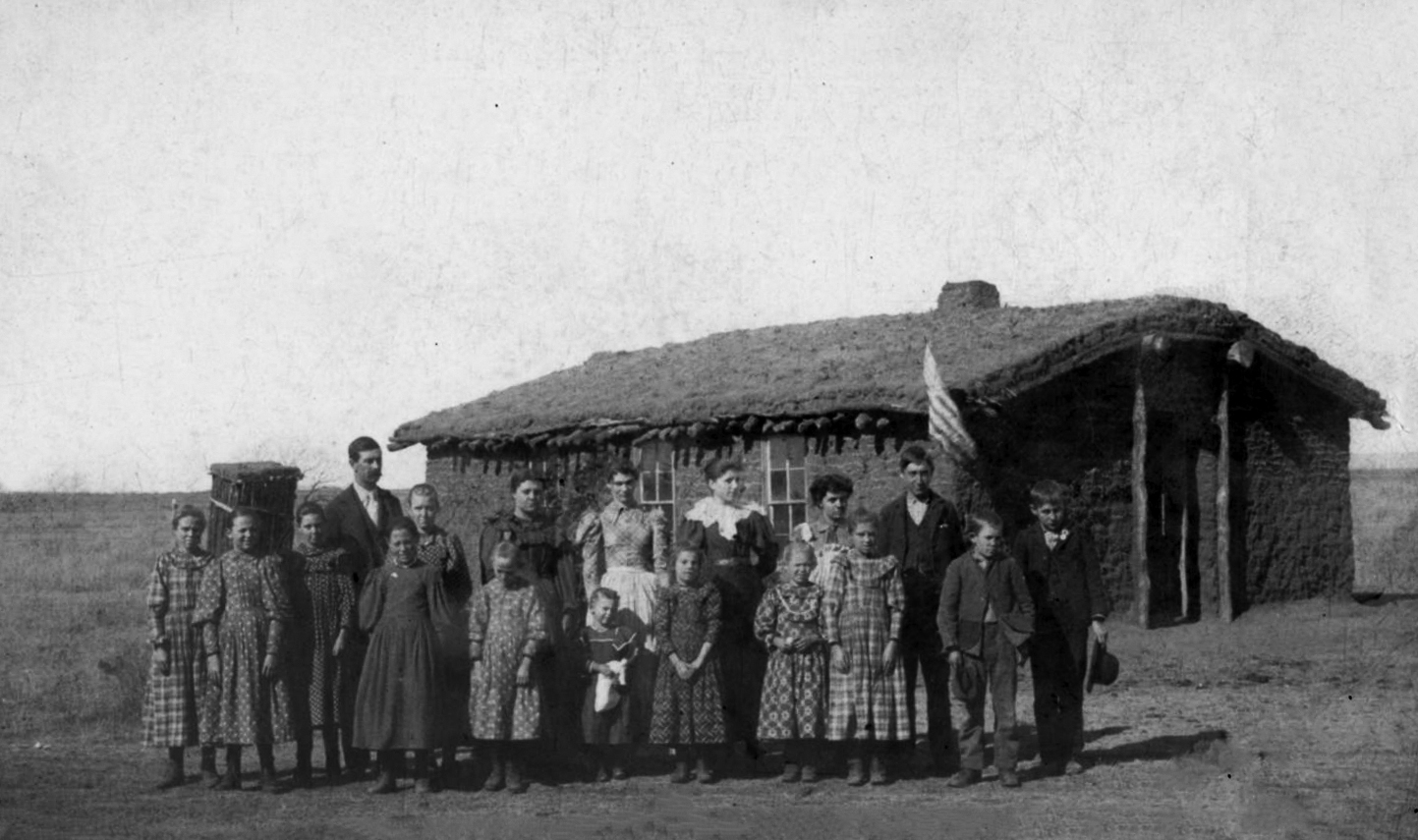 People stand outside a small structure made of sod bricks