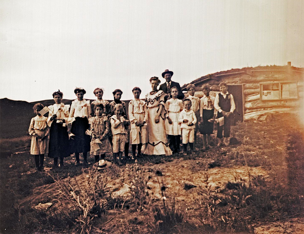 A group photograph in front of a school dug into the ground with a roof covering