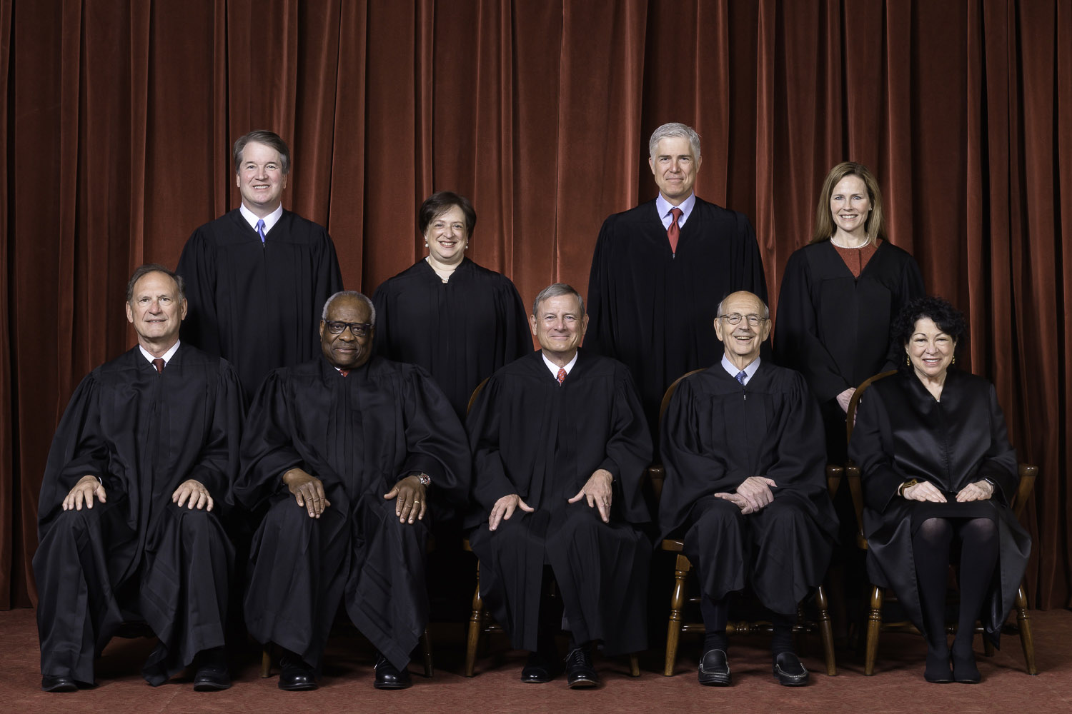 A formal portrait of the justices of the Supreme Court in their black robes in front of a dark red curtain.